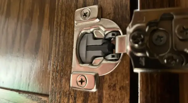 Dettaglio di una cerniera ammortizzata per ante cucina in legno scuro, con viti a vista.