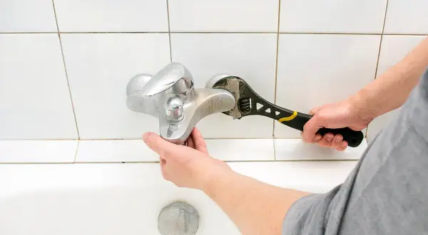Mano con chiave inglese ripara un rubinetto cucina perde.