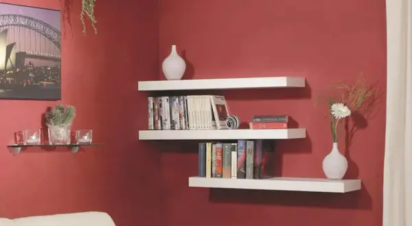 Mensole bianche a muro con libri, vasi e una pianta. Una guida visiva su come montare una mensola.