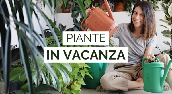 Donna sorridente con annaffiatoi, circondata da piante rigogliose. Impara come innaffiare le piante quando si va in vacanza per mantenerle sane.