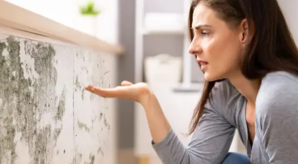 Donna preoccupata osserva muffa su muro. Scopri come togliere umidità in casa per un ambiente più sano.