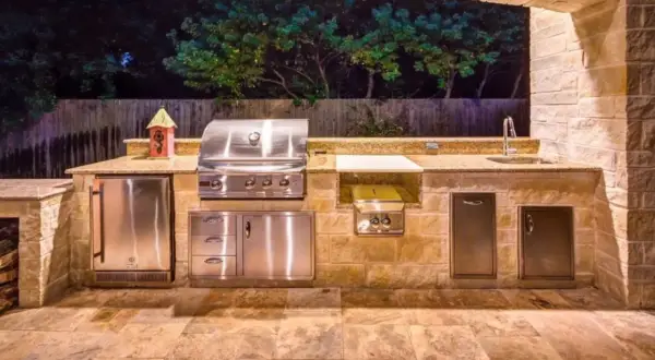 Cucina esterna in muratura fai da te con barbecue, frigo, lavello e piano di lavoro in granito.