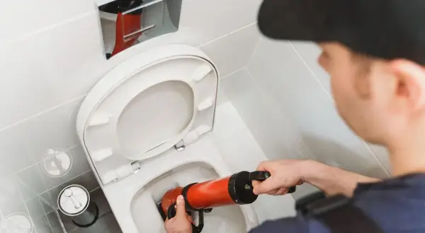Un idraulico usa uno sturalavandini per liberare un WC. Un filo d'acqua scende nel water, pronto per essere liberato.