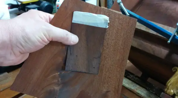 Mano che tiene un pezzo di impiallacciatura di legno scuro, pronto per restaurare un mobile impiallacciato.