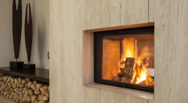 Un camino moderno con fiamme vive, pronto per lo spazzacamino. Legna accatastata e sculture decorative completano l'arredo.