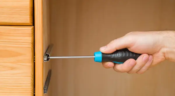 Mano con cacciavite che lavora su guide per cassetti in legno.