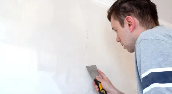 Uomo con spatola ripara una crepa su un muro scrostato, pronto a stuccare.
