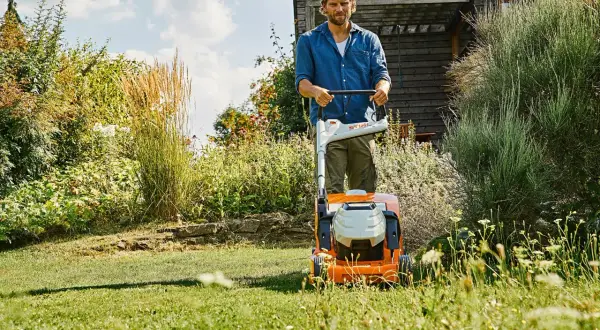 Uomo con tosaerba elettrico in un giardino rigoglioso. Il sole splende, un momento ideale per prendersi cura del prato, ma quando innaffiare il prato?