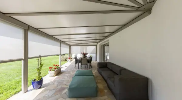 Telo per pergolato fissato con sistema a scomparsa, creando un'area relax con divano e tavola da pranzo.