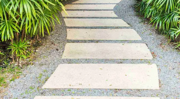 Un sentiero sinuoso in lastre di pietra su ghiaia, un'idea per come pavimentare un giardino senza cemento, circondato da vegetazione lussureggiante.