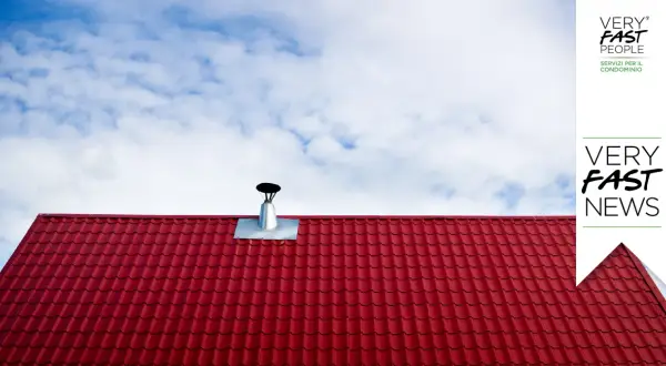 Tegole rosse e canna fumaria su tetto, per la manutenzione canna fumaria privata in condominio. Cielo azzurro con nuvole bianche.