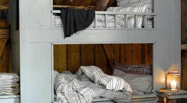 Accogliente letto a castello fai da te in legno grezzo, con coperte a quadri e a righe, perfetto per un rifugio rustico.