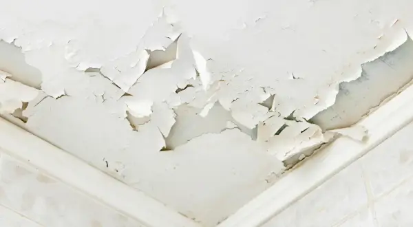 Soffitto scrostato e macchiato, segnale evidente di come riconoscere le infiltrazioni d'acqua. La pittura si stacca a chiazze, rivelando l'umidità sottostante.