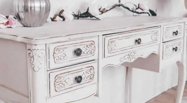 Un tavolo da toeletta bianco, con dettagli intagliati e un effetto invecchiato, pronto per essere restaurato in stile shabby.