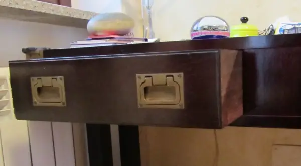 Cassetti che non scorrono, con maniglie dorate su un mobile scuro. Sul piano, oggetti decorativi e libri.