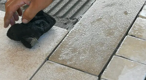 Mano che pulisce le fughe tra le piastrelle bagnate, evidenziando possibili errori posa piastrelle.
