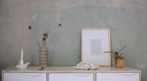 Parete con effetto materico, ideale per chi vuole imparare come pitturare una parete con stile. Arredamento minimalista con vasi, candela e quadro.