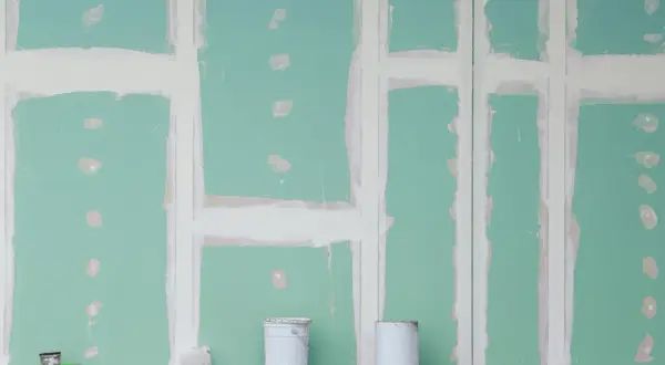 Parete in cartongesso verde con stuccatura delle giunture. Due secchi bianchi in primo piano, detriti sul pavimento. Le misure lastre cartongesso sono fondamentali per questo lavoro.