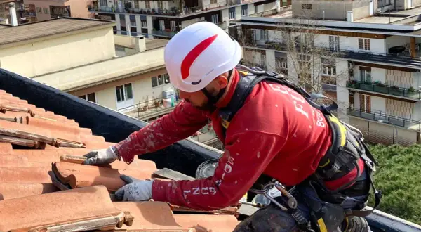 Operaio con imbracatura lavora sul tetto per isolare tetto senza togliere tegole, applicando materiale isolante.