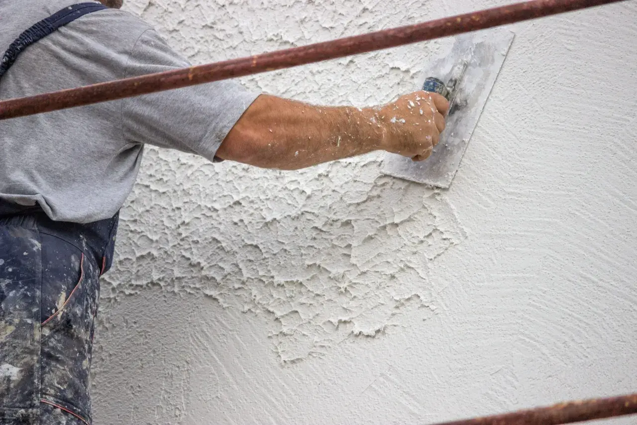 Mano di un operaio che applica la finitura intonaco rustico con una spatola, creando una texture irregolare e caratteristica.