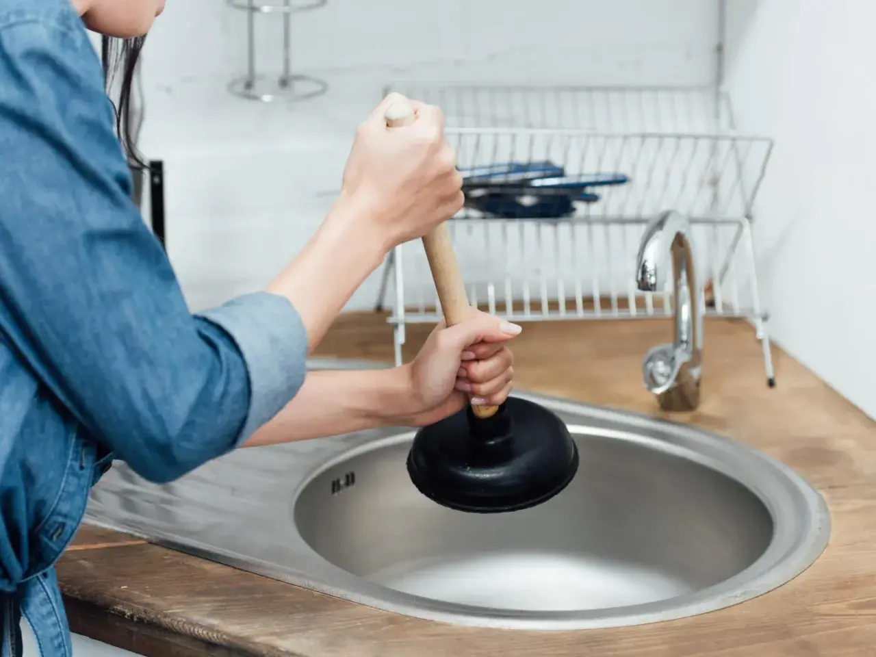 Mani che usano uno sturalavandini per sturare il lavandino intasato in cucina.