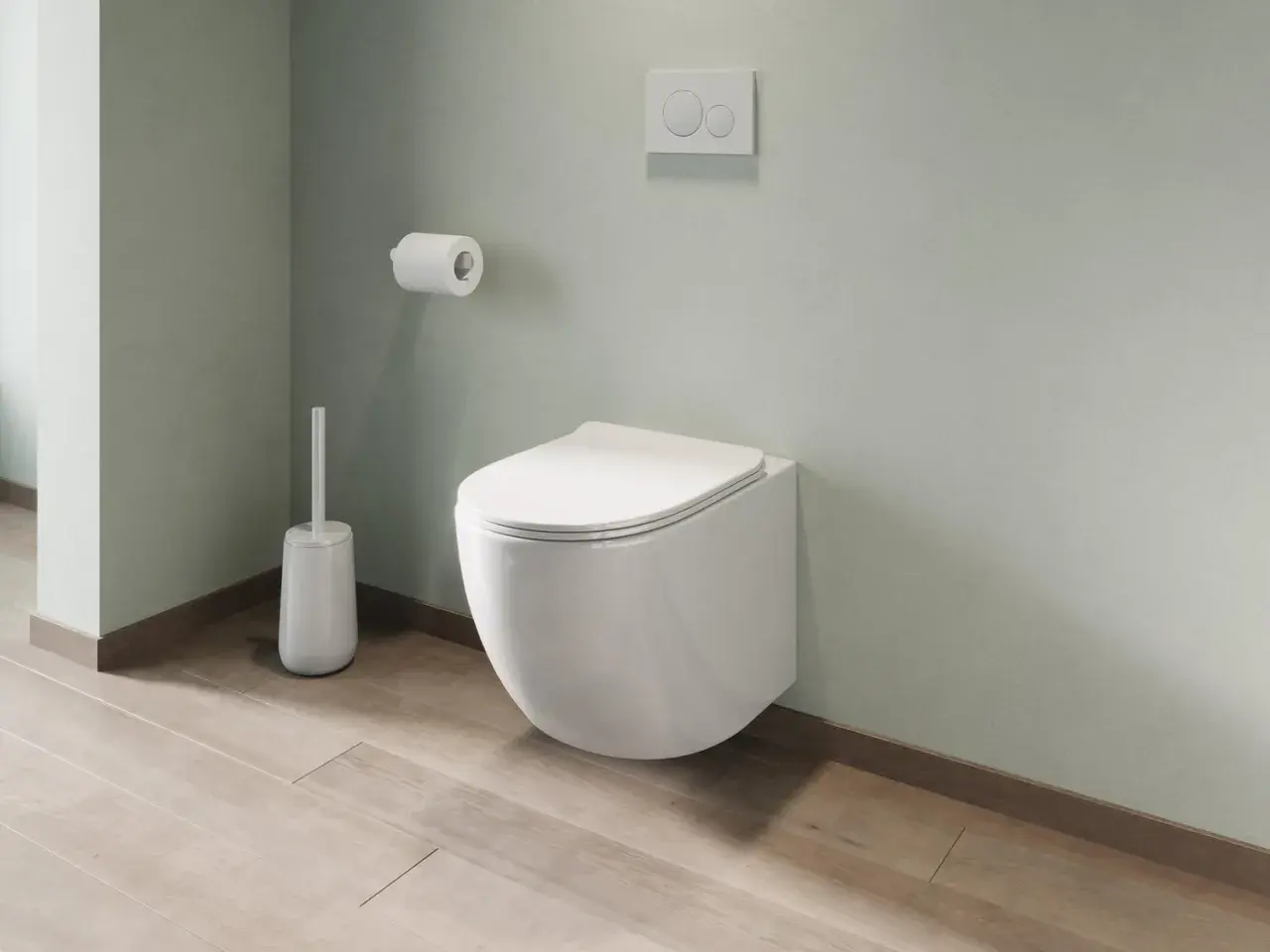 Un moderno bagno con montaggio sanitari sospesi: water a parete, scopino bianco e rotolo di carta igienica su parete verde pastello.