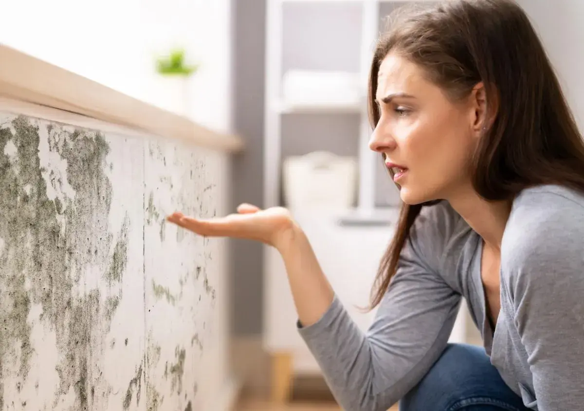 Donna preoccupata osserva muffa su muro. Scopri come togliere umidità in casa per un ambiente più sano.