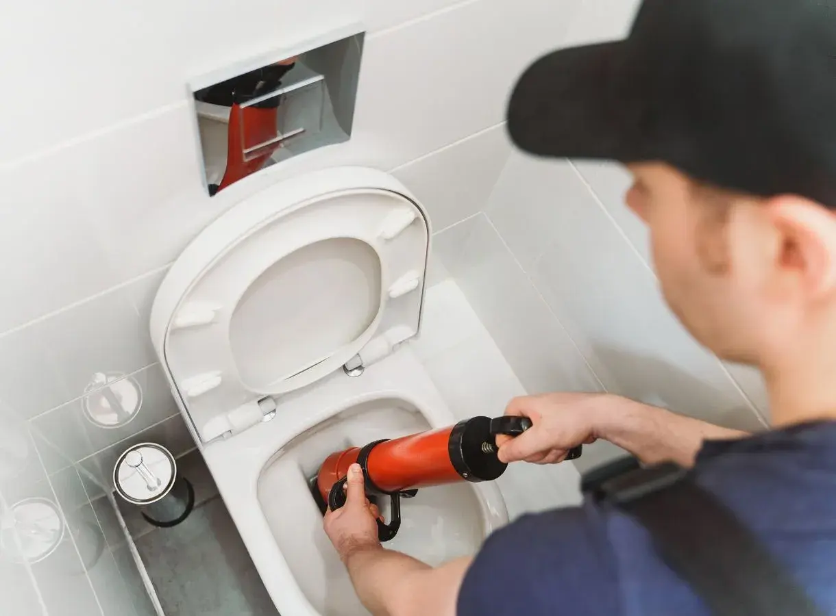 Un idraulico usa uno sturalavandini per liberare un WC. Un filo d'acqua scende nel water, pronto per essere liberato.