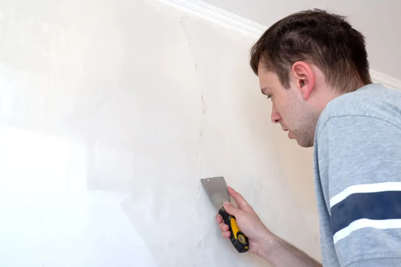 Uomo con spatola ripara una crepa su un muro scrostato, pronto a stuccare.