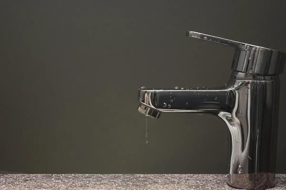 Rubinetto che perde, gocce d'acqua scivolano sul metallo lucido.