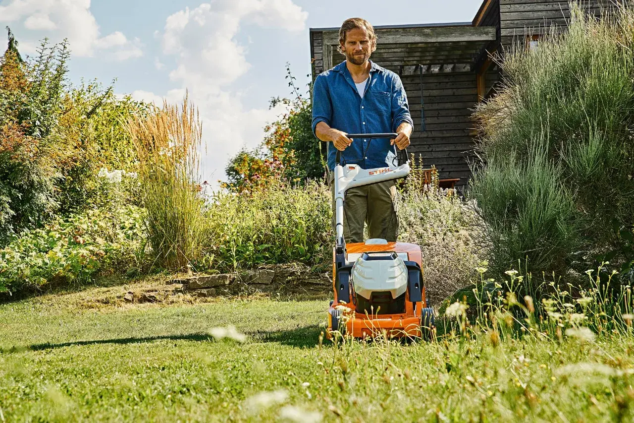 Uomo con tosaerba elettrico in un giardino rigoglioso. Il sole splende, un momento ideale per prendersi cura del prato, ma quando innaffiare il prato?