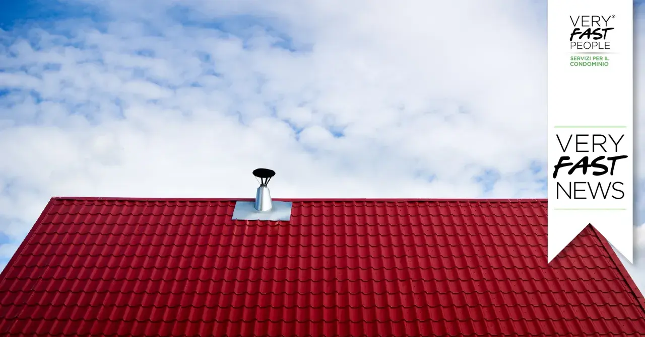 Tegole rosse e canna fumaria su tetto, per la manutenzione canna fumaria privata in condominio. Cielo azzurro con nuvole bianche.