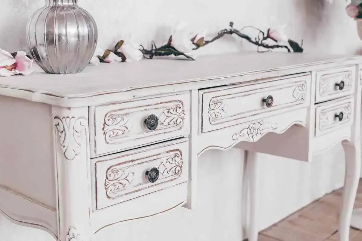Un tavolo da toeletta bianco, con dettagli intagliati e un effetto invecchiato, pronto per essere restaurato in stile shabby.