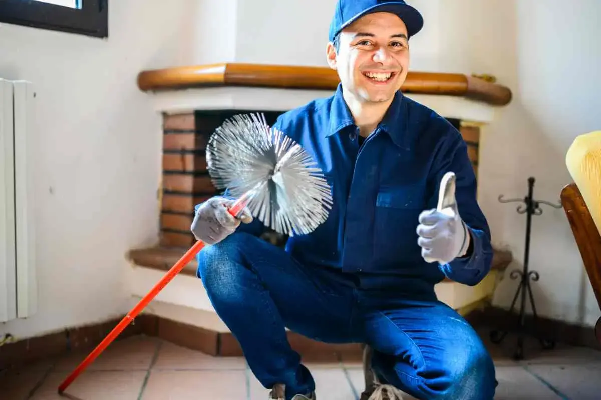 Un tecnico sorridente mostra una spazzola per camino, pronto per insegnare come pulire la canna fumaria del camino.