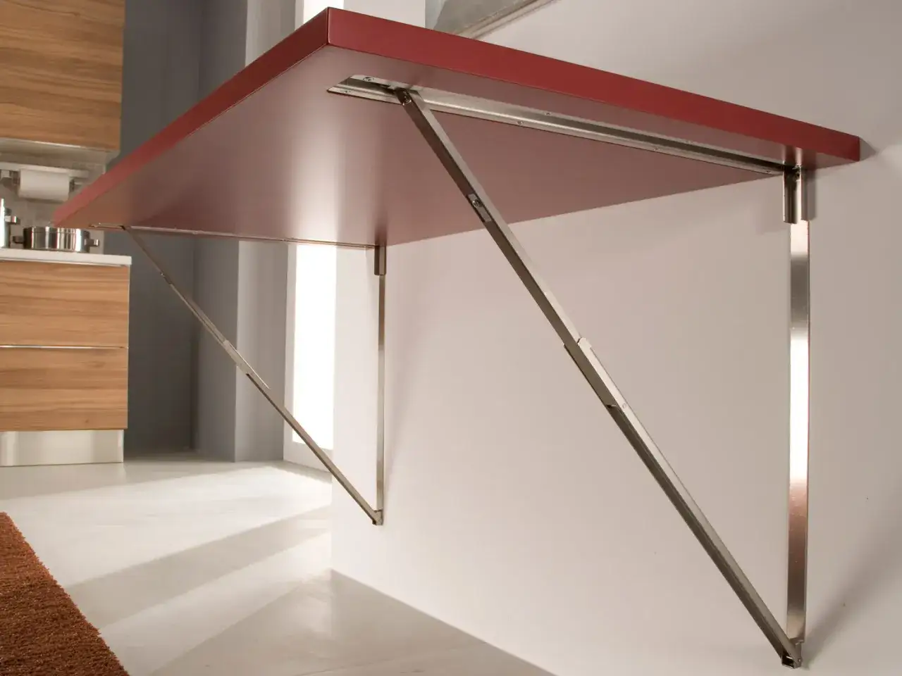 Tavolo pieghevole fai da te, con piano rosso e staffe metalliche a scomparsa, ideale per ottimizzare gli spazi in cucina.