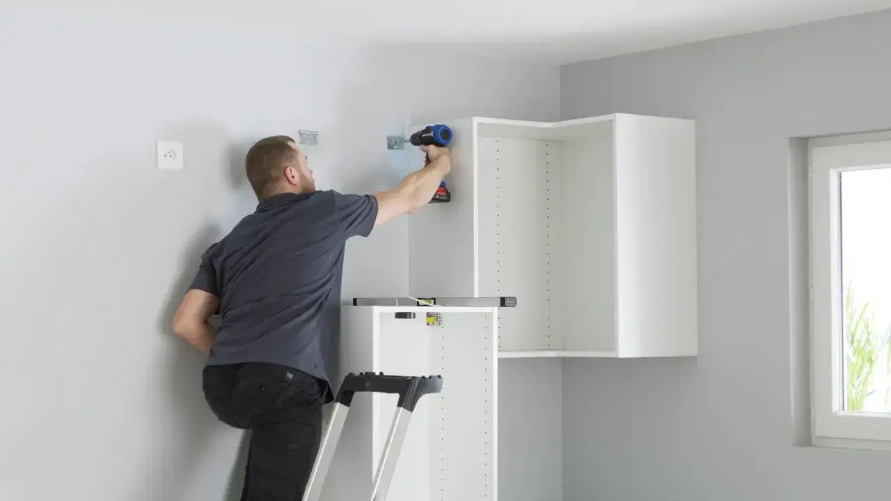 Uomo su scala avvita pensili cucina bianchi al muro. Guida pratica su come appendere i pensili della cucina.