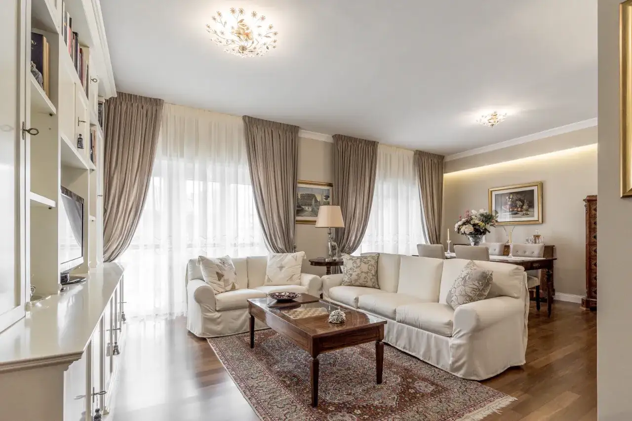 Tende eleganti scendono dal soffitto, creando un'atmosfera accogliente nel soggiorno con divani bianchi e un tavolino in legno.