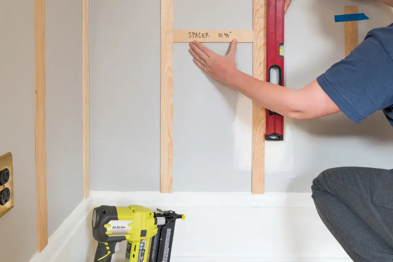Persona usa livella e listello di legno per segnare la posizione, mostrando come fissare listelli di legno al muro con precisione. Attrezzi da lavoro a portata di mano.
