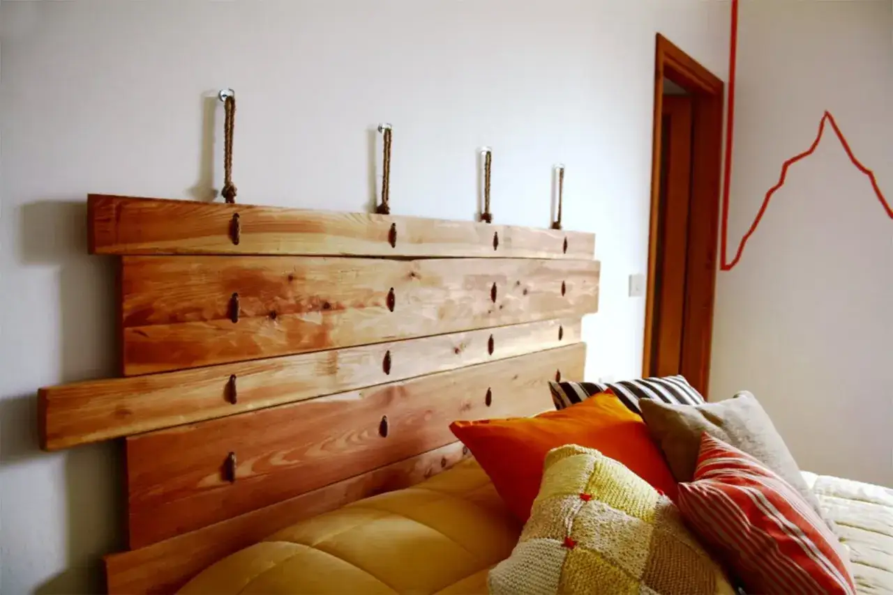Testiera letto fai da te in legno grezzo, appesa al muro con corde. Un tocco rustico e originale per la camera da letto.