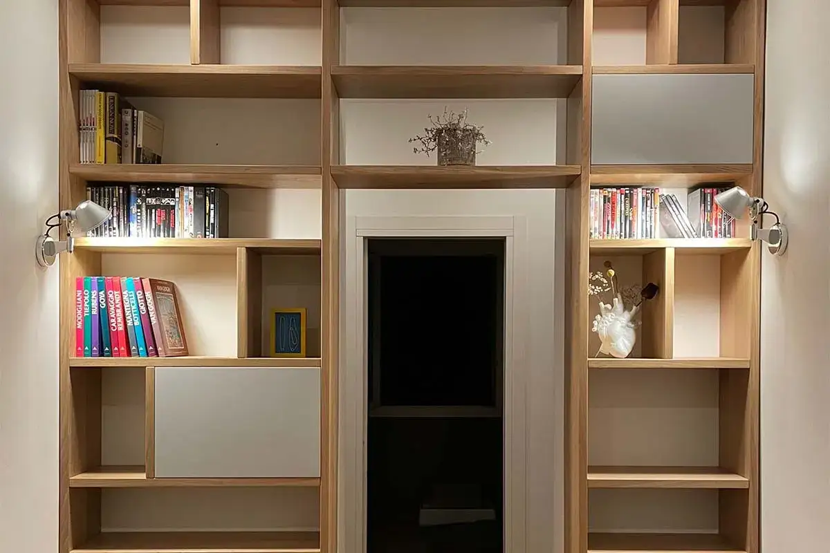 Una libreria fai da te in legno chiaro, piena di libri e oggetti decorativi, con luci direzionabili.