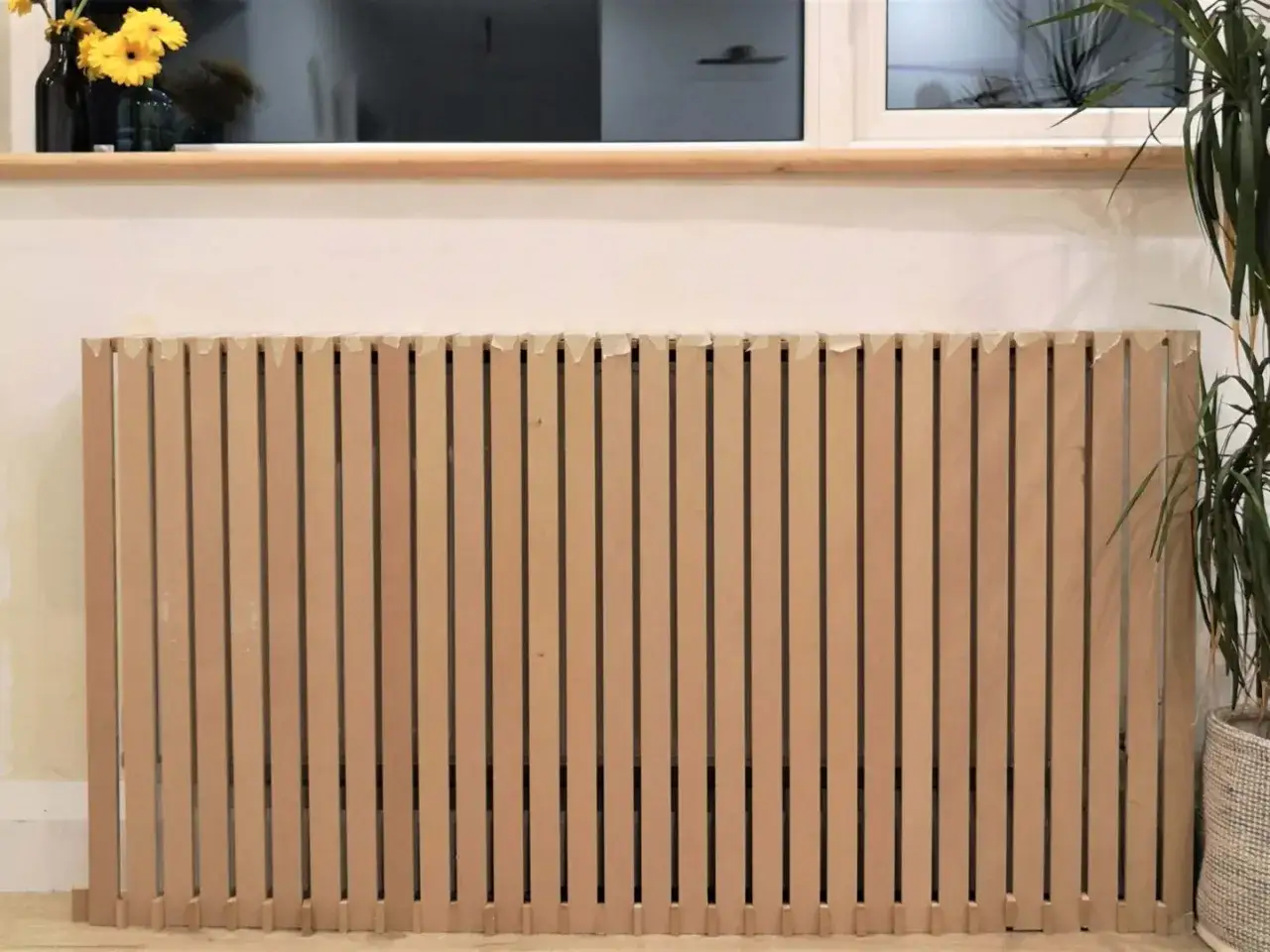 Un copritermosifoni fai da te in legno grezzo, con listelli verticali, pronto per essere installato.