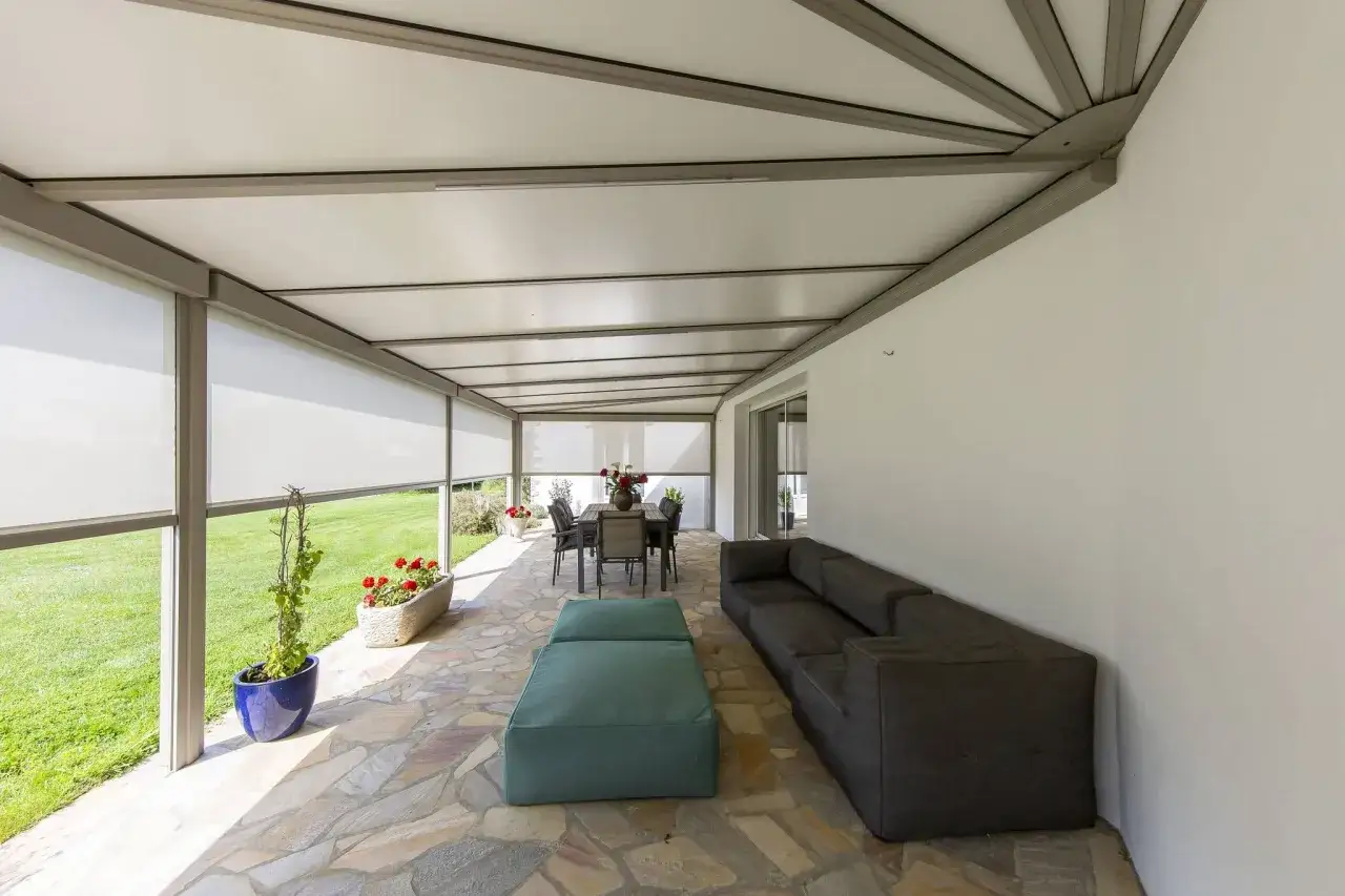 Telo per pergolato fissato con sistema a scomparsa, creando un'area relax con divano e tavola da pranzo.