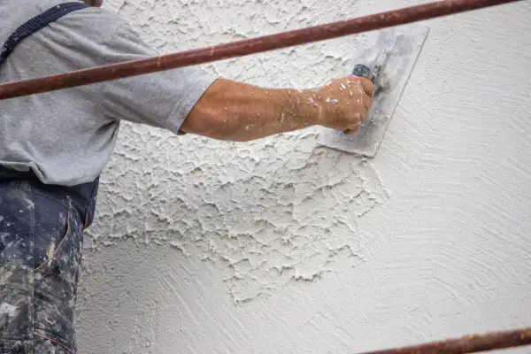 Mano di un operaio che applica la finitura intonaco rustico con una spatola, creando una texture irregolare e caratteristica.