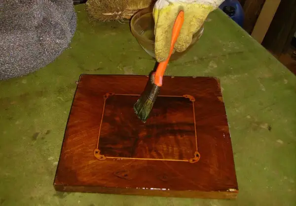 Guanto giallo applica liquido con pennello su un mobile in legno intarsiato. Inizia il processo per come sverniciare un mobile.