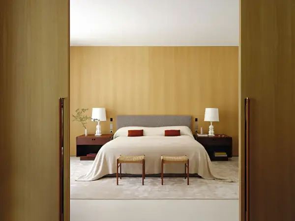 Camera da letto con letto centrale, testiera grigia, comodini in legno scuro e due sgabelli. Ottima idea su come posizionare il letto in camera per un look armonioso.