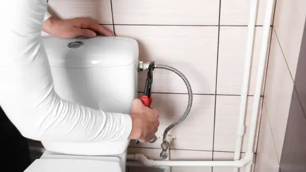 Mani con pinza che lavorano sul tubo flessibile per chiudere acqua cassetta wc.