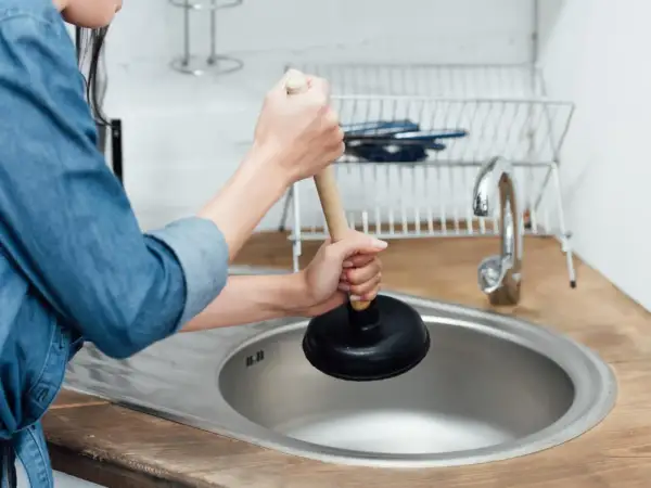 Mani che usano uno sturalavandini per sturare il lavandino intasato in cucina.