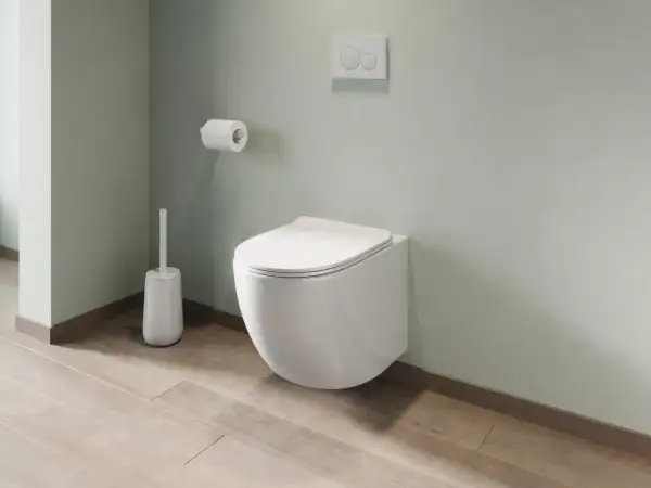 Un moderno bagno con montaggio sanitari sospesi: water a parete, scopino bianco e rotolo di carta igienica su parete verde pastello.