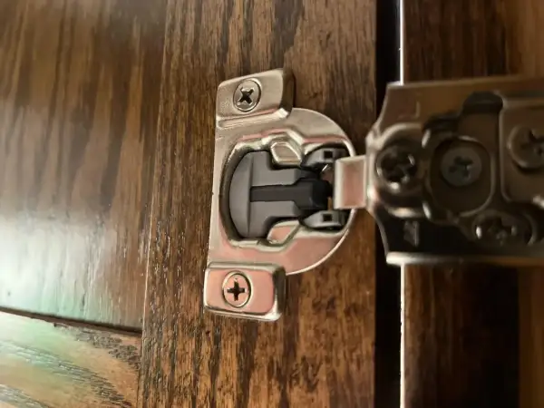 Dettaglio di una cerniera ammortizzata per ante cucina in legno scuro, con viti a vista.