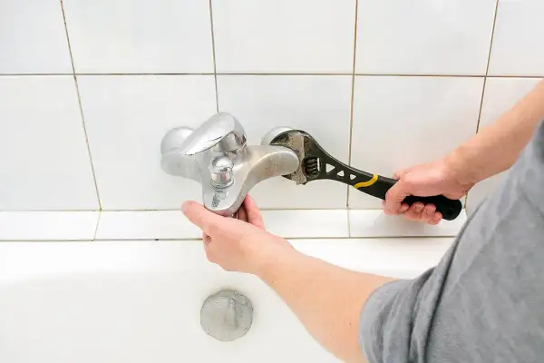 Mano con chiave inglese ripara un rubinetto cucina perde.